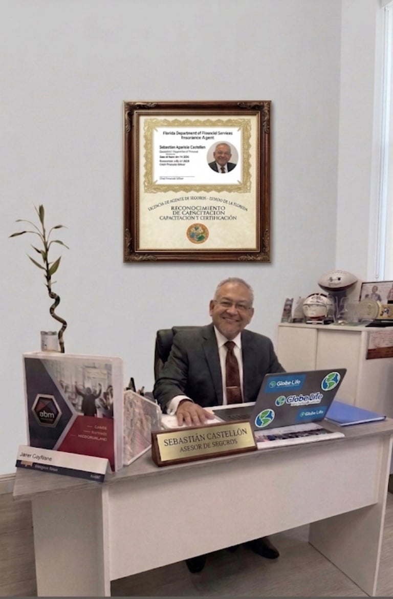 Professional man in business suit seated at white desk with nameplate, laptop, and office items, with framed certificate on wall behind
